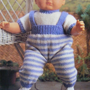 Puede incluir: Un conjunto de muñeca de punto con un patrón de rayas blancas y azules. El conjunto tiene un babero de punto azul y una camisa de punto blanca con ribete azul. La muñeca lleva zapatos blancos.