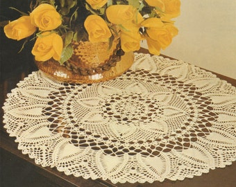 May include: A white crocheted doily with a delicate floral design. The doily is placed on a dark wooden surface with a bouquet of yellow roses in a brown ceramic vase.