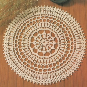 Könnte beinhalten: Eine weiße Häkeldeckchen mit einem zarten Blumenmuster. Das Deckchen ist rund und hat einen Durchmesser von etwa 30 cm.