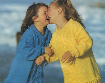 May include: Two young girls wearing knitted sweaters, one in blue and one in yellow, are laughing and holding hands. The girl in the blue sweater is wearing yellow pants, and the girl in the yellow sweater is wearing blue pants.