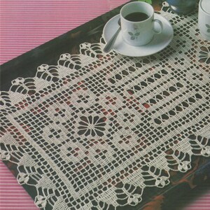 May include: A white crocheted doily with a delicate floral design in the center. The doily is placed on a black tray with a cup of coffee and a saucer.