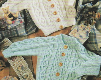 May include: Two knitted baby cardigans with cable knit patterns. One cardigan is white with a light purple stripe and the other is light blue with a light green stripe. Both cardigans have wooden buttons.
