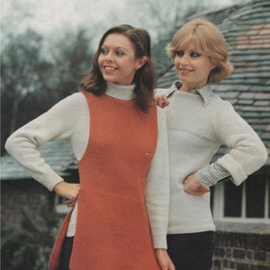May include: Two women wearing knitted sweaters. The woman on the left is wearing a white sweater with a long, orange vest over it. The woman on the right is wearing a white sweater with a white and black plaid shirt underneath.