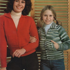 May include: Two people wearing knitted zip-up sweaters. The woman on the left is wearing a red sweater and the woman on the right is wearing a green and white striped sweater.