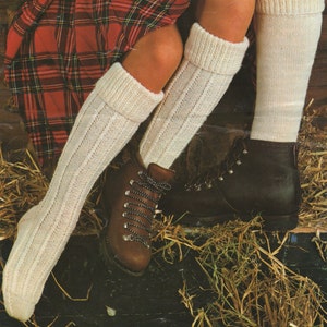 Può includere: Un paio di calze bianche a maglia fino al ginocchio con un motivo a costine. Le calze sono indossate con stivali da trekking in pelle marrone.