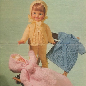 May include: A set of three knitted doll clothes, including a pink hooded robe, a yellow cardigan and trousers set, and a blue dress. The doll clothes are made with a textured knit stitch.