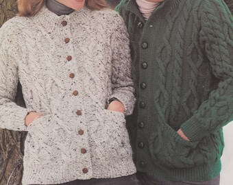 May include: A couple wearing knitted sweaters. The woman is wearing a light gray sweater with a cable knit pattern and the man is wearing a dark green sweater with a cable knit pattern. Both sweaters have buttons down the front.