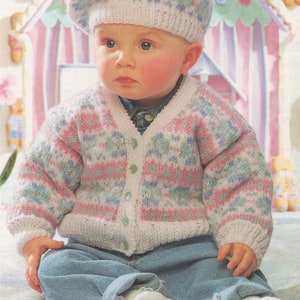 May include: A baby wearing a pink, blue, and white knitted cardigan with a matching beret. The cardigan has a button closure and the baby is sitting on a light blue blanket.