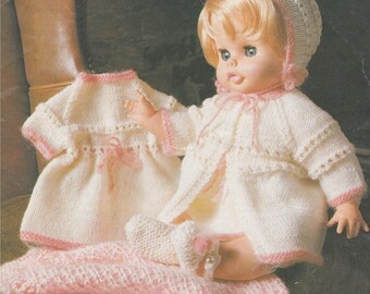 May include: A knitted doll outfit set in white and pink. The set includes a dress, a cardigan, a hat, and booties. The outfit is designed for a doll with a 12-inch body.