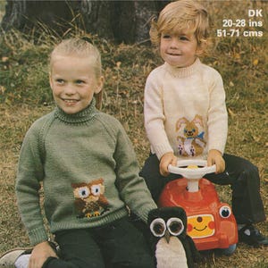 May include: Two children wearing knitted sweaters with animal designs. The girl is wearing a green sweater with an owl design and the boy is wearing a white sweater with a bunny design. The boy is sitting on a red toy car.