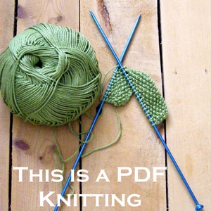 Peut inclure: Une pelote de laine verte, deux aiguilles &agrave; tricoter bleues et un morceau de tissu vert tricot&eacute; en partie sur une surface en bois. Le texte "THIS IS A PDF KNITTING PATTERN" est imprim&eacute; sous la laine et les aiguilles.