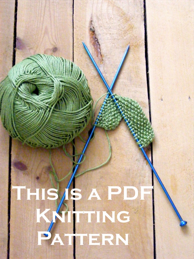 Peut inclure: Une pelote de laine verte, deux aiguilles &agrave; tricoter bleues et un morceau de tissu vert tricot&eacute; en partie sur une surface en bois. Le texte "THIS IS A PDF KNITTING PATTERN" est imprim&eacute; sous la laine et les aiguilles.