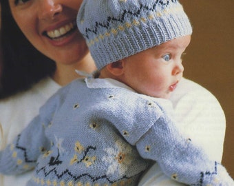 May include: A baby wearing a blue knitted sweater with a floral pattern and a matching blue knitted hat with a yellow pom-pom.