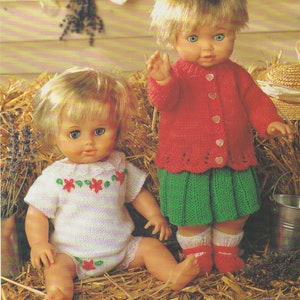 Puede incluir: Dos muñecas con atuendos tejidos. La muñeca de la izquierda lleva un vestido tejido a rayas blancas y rosas con flores rojas. La muñeca de la derecha lleva una chaqueta de punto roja con una falda de punto verde y calcetines de punto rojos.