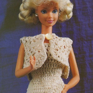 May include: A crocheted dress and matching bolero for a doll. The dress and bolero are cream colored and have a delicate floral pattern. The doll has blonde hair and blue eyes.