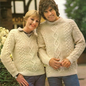 Könnte beinhalten: Zwei Personen tragen cremefarbene Strickpullover mit Zopfmuster. Die Pullover haben ein Rautenmuster und sind aus einem dicken Garn gefertigt.