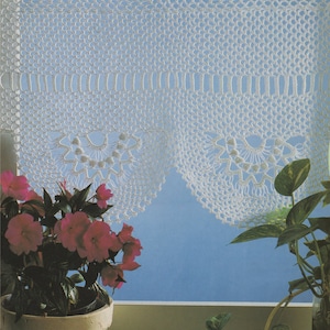 May include: White crocheted window valance with a scalloped edge and a delicate floral design. The valance is hung on a metal rod with yellow ribbon ties. Two potted plants are in the foreground.