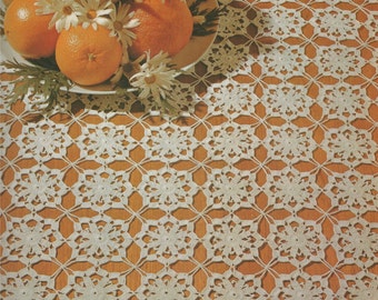 May include: A white crocheted tablecloth with a square pattern. A white plate with oranges, pears, and white flowers sits on top of the tablecloth.