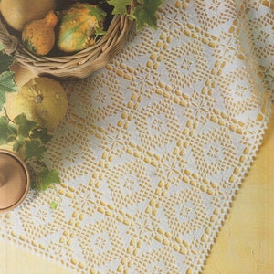 Könnte beinhalten: Ein weißer gehäkelter Tischläufer mit einem zarten Blumenmuster. Der Läufer liegt auf einer gelben Oberfläche und hat einen gewellten Rand.