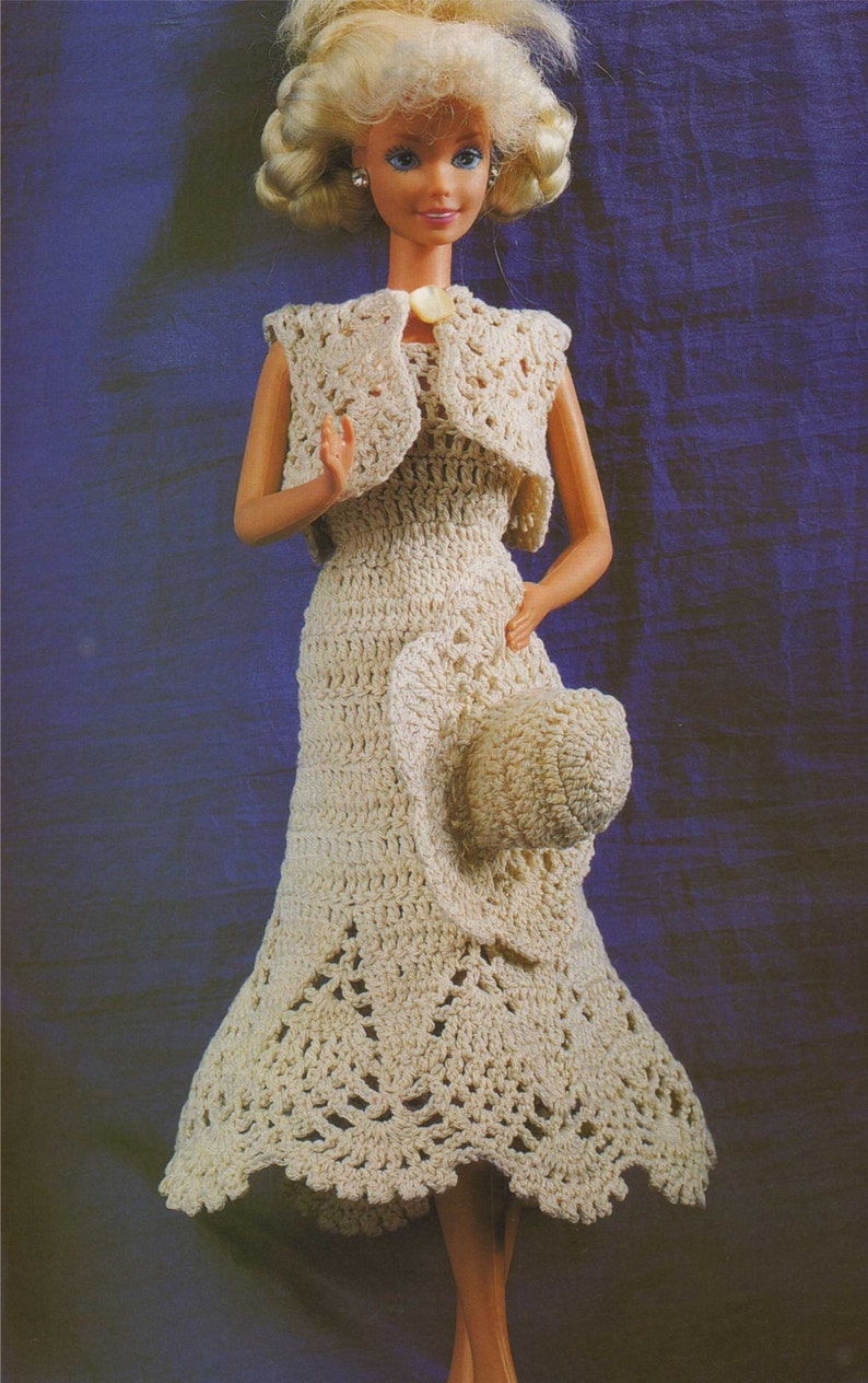 May include: A crocheted dress and hat set in a cream color. The dress has a fitted bodice and a flowing skirt with a scalloped hem. The hat is a wide-brimmed sun hat with a crocheted design.