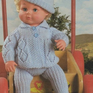 Puede incluir: Un conjunto de muñeca de punto azul con un gorro de punto azul a juego. La muñeca está sentada en un carro de juguete de madera con ruedas rojas.