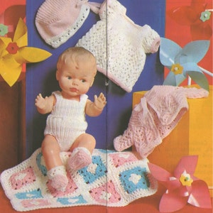 May include: A crocheted baby doll outfit set with a pink and white dress, a pink hat, and a pink and white blanket. The set is displayed on a red surface with a doll sitting on the blanket.