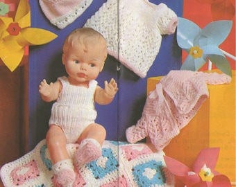 May include: A crocheted baby doll outfit set with a pink and white dress, a pink hat, and a pink and white blanket. The set is displayed on a red surface with a doll sitting on the blanket.