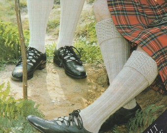 Op de afbeelding: Twee paar witte gebreide sokken met een kabelbreipatroon. De sokken worden gedragen met zwarte leren schoenen. De tekst "KILT HOSE" is zichtbaar in de rechterbenedenhoek van de afbeelding.