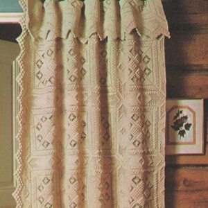 May include: A white crocheted curtain with a scalloped edge and a geometric pattern. The curtain is hung on a wooden rod with gold hooks.