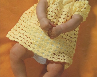May include: A baby wearing a yellow crocheted dress and matching yellow crocheted shoes. The baby is smiling and lying on a yellow blanket.