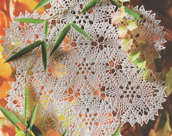 May include: A white crocheted doily with a delicate floral pattern, resting on a bed of autumn leaves.