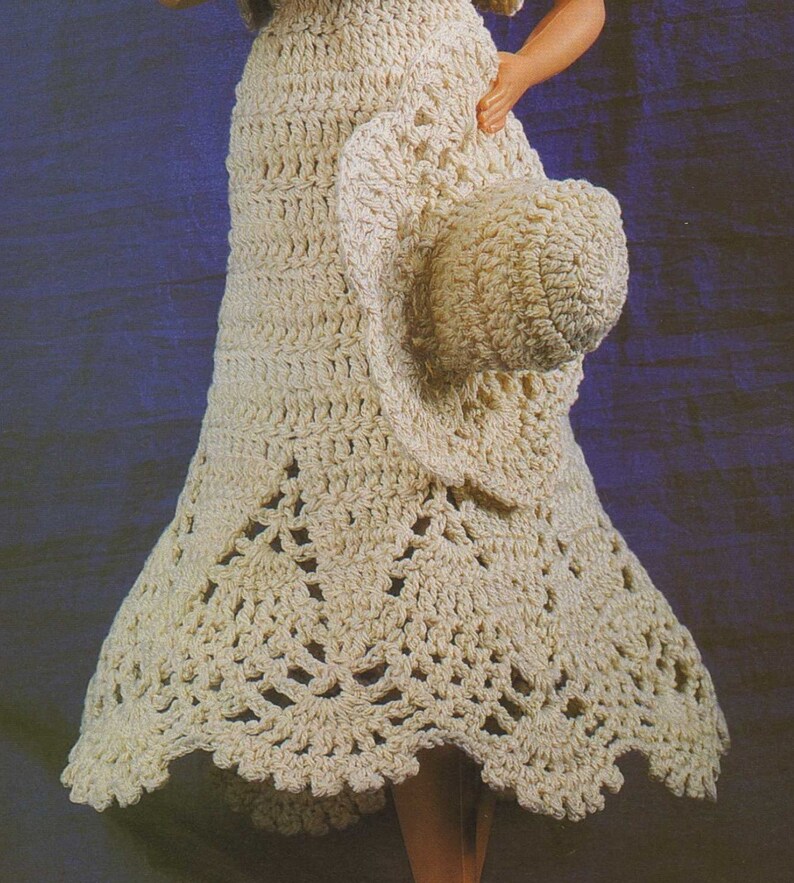 May include: A crocheted dress and hat set in a cream color. The dress has a flared skirt with a scalloped hem. The hat is a wide-brimmed sun hat.