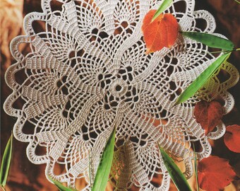 May include: A cream-colored, handmade crochet doily with an intricate, openwork design. The doily is circular, with a scalloped edge. Red and orange leaves and green bamboo stalks surround the doily, creating a natural, autumnal aesthetic.