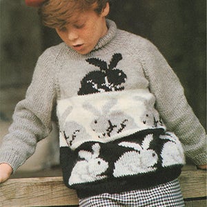 May include: A gray knitted sweater with a black and white bunny rabbit design. The sweater has a turtleneck and long sleeves. The boy is wearing a red beret.