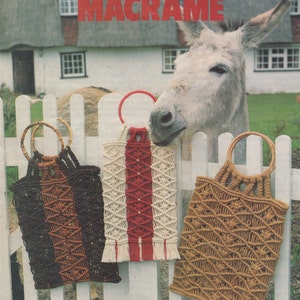 May include: Three macrame bags with different colored cords hanging on a white picket fence. The bags have wooden and metal handles. A donkey is peeking over the fence.