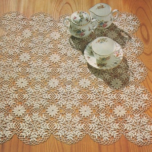 May include: A white crocheted doily with a delicate floral pattern. The doily is laid out on a wooden surface with three porcelain teacups and saucers.