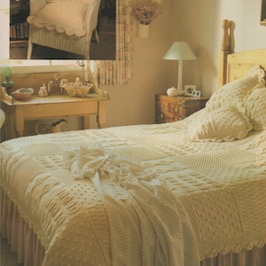 May include: A white wicker chair with a crocheted cushion sits in a room with a white wicker bed with a crocheted bedspread and pillows. The room has a light brown wooden dresser with a lamp on top.