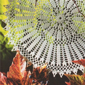 May include: A white crocheted doily with a delicate floral pattern, resting on a bed of autumn leaves.