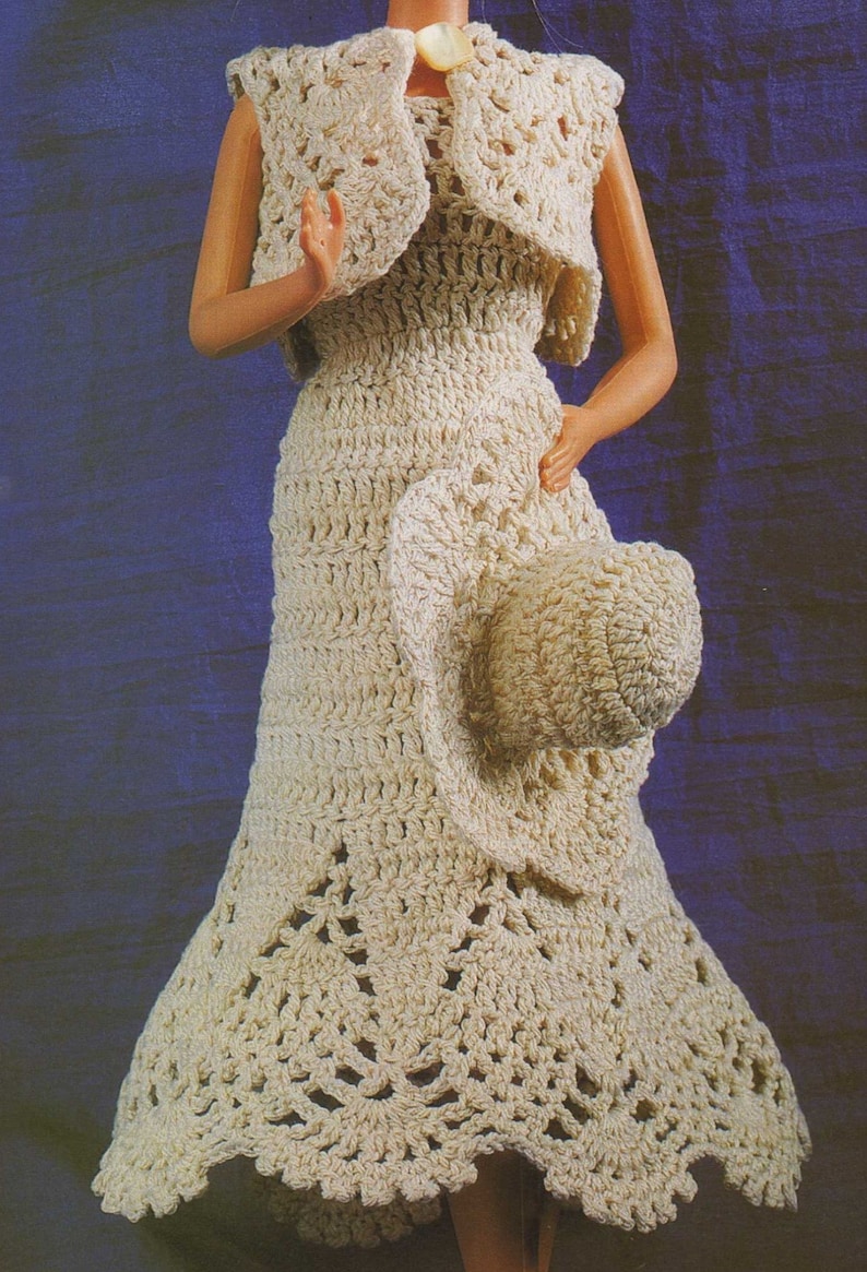 May include: A crocheted dress and matching hat set in a cream color. The dress has a sleeveless bodice and a flowing skirt with a scalloped hem. The hat is a wide-brimmed sun hat.
