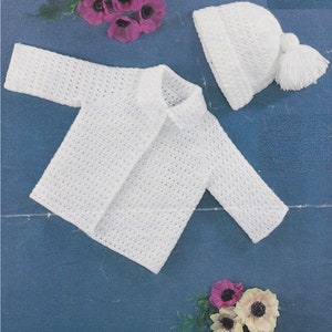 May include: White crocheted baby cardigan and hat set. The cardigan has a button closure and the hat has a pompom.