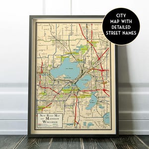 May include: Framed vintage map of Madison, Wisconsin, with detailed street names. The map features a beige background with blue lakes and red roads. The text "New Road Map of Madison Wisconsin" is visible at the bottom. A black circle with white text reads "City Map with Detailed Street Names".