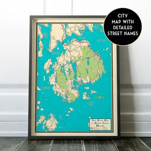May include: Framed map of Mount Desert Island, Maine, with detailed street names. The map features a teal blue background with green and beige landmasses, and red road markings. The frame is dark gray.
