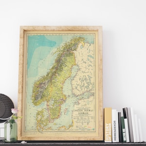 May include: A vintage map of Scandinavia, framed in a light wood frame. The map shows Sweden, Norway, and Denmark in detail, with a color scheme of green, yellow, and blue. The map is titled "Letts Popular Atlas" and includes a key for understanding the map's symbols.