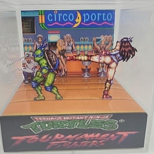 May include: A Teenage Mutant Ninja Turtles diorama featuring Leonardo and a female character in a fighting pose. The scene is set in a bar with patrons and the text "Circo Porto" above. The base of the diorama has the game title "Tournament Fighters".