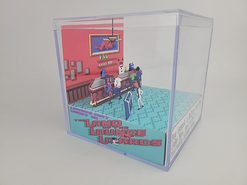 Puede incluir: Diorama en miniatura de una escena de bar dentro de una caja de pl&aacute;stico transparente. La escena presenta figuras pixeladas, una barra y un letrero que dice "The Land of the Lounge Lizards". El fondo es rojo con arte enmarcado.
