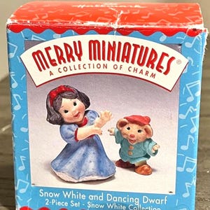 Könnte beinhalten: Ein Box-Set von "Merry Miniatures" mit Schneewittchen und einer tanzenden Zwergfigur. Die blaue Box zeigt Noten und die Figuren tragen ein blau-weißes Kleid und einen blauen Mantel mit roter Mütze. Auf der Box steht "Snow White and Dancing Dwarf".