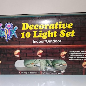 Puede incluir: Juego decorativo de 10 luces para uso interior/exterior. La caja presenta el logotipo "Tropix" y texto. El juego incluye 10 luces, bombillas de repuesto y mide aproximadamente 3 metros de largo. La caja tiene un diseño de pared de ladrillo.