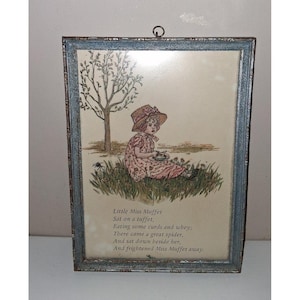 Puede incluir: Impresión vintage enmarcada que representa a una niña con un vestido y sombrero rosas, sentada en un área cubierta de hierba cerca de un árbol. La impresión incluye el poema "Little Miss Muffet" en un marco decorativo con un acabado azul grisáceo. Un anillo metálico decorativo en la parte superior.