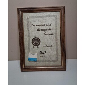 May include: A rectangular document and certificate frame with a dark brown wood grain finish. The insert features the text "All Purpose Document and Certificate Frame", "Full Strength Glass", "Intercraft", and "5x7". A blue and white price tag is attached.