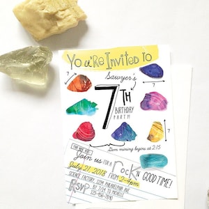 May include: A birthday party invitation with colorful gemstone illustrations. The invitation reads "You're Invited to Sawyer's 7th Birthday Party!" with event details. Decorative rocks are placed around the invitation.
